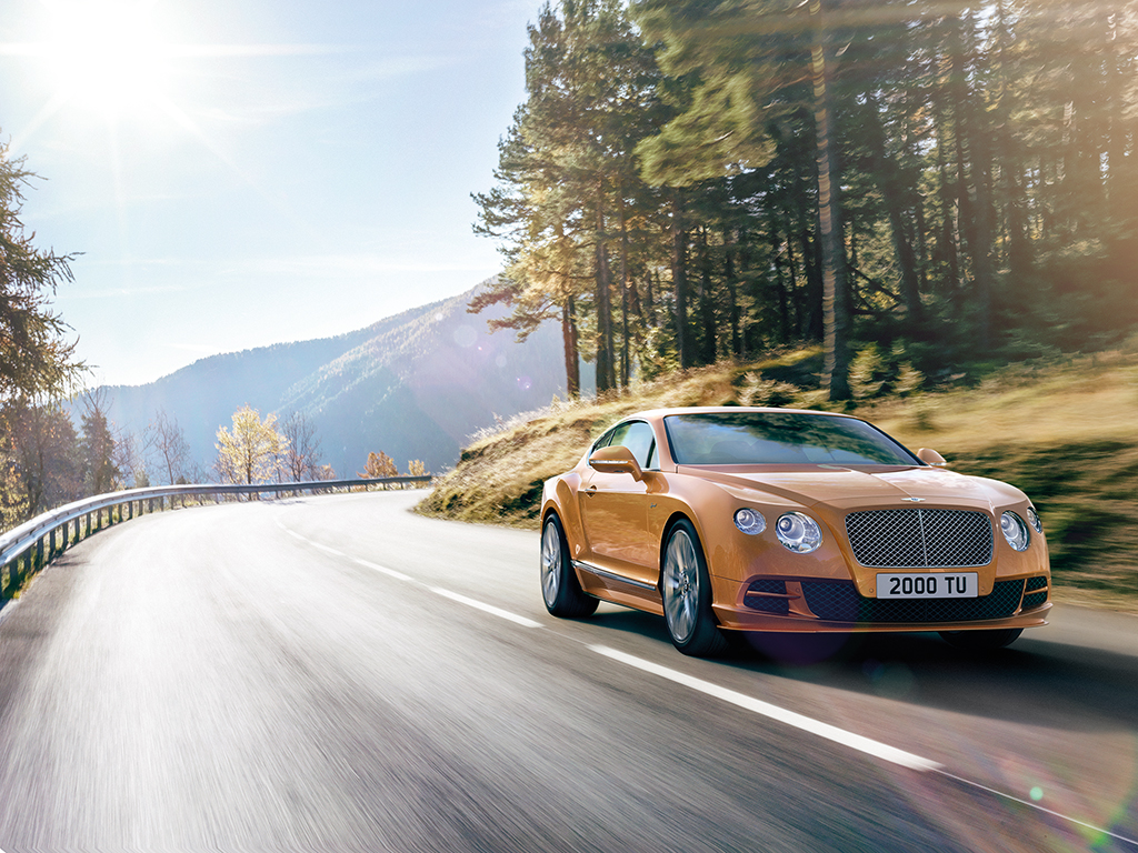 Bentley Gold driving on road by trees and mountain CGI
